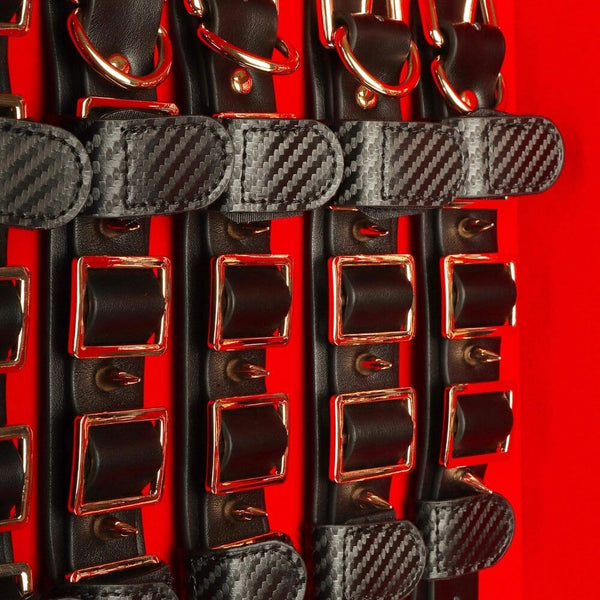 Coffret BDSM ouvert en cuir noir avec intérieur rouge, présentant un ensemble d’accessoires assortis comprenant menottes, sangles, cravaches et chaînes, disposés de manière ordonnée dans une esthétique luxueuse.