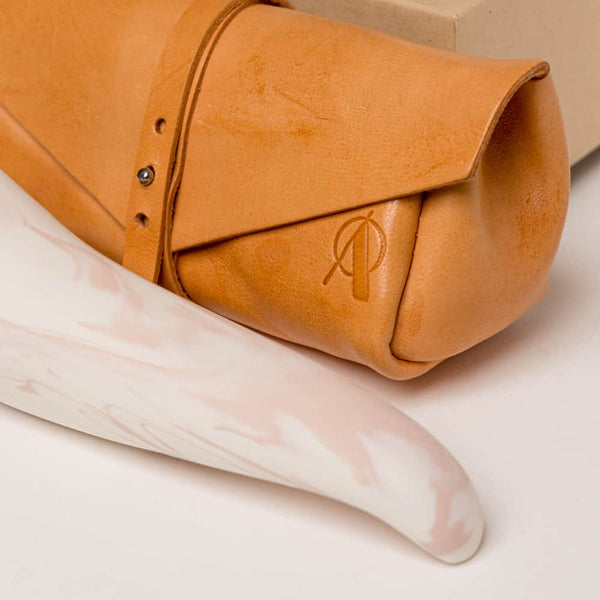 Pochette en cuir orangé avec le logo de la marque dessus .The spur épais sur le haut et embout plus fin, il est de porcelaine de couleur rose et blanc de Adeles brydges chez brigade mondaine