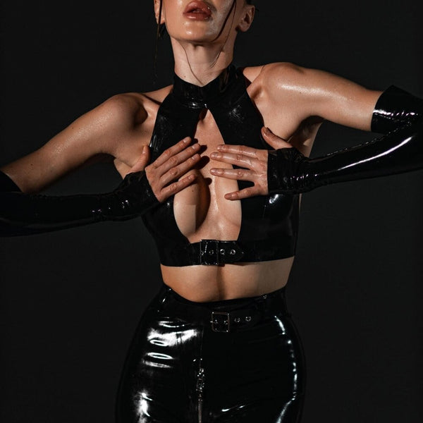 Ensemble en latex noir ANOESES avec top à col montant, short taille haute et gants longs assortis, porté par un modèle en position accroupie sur fond sombre.