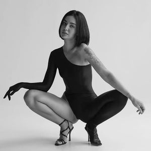 Catsuit DEXTRA ANOESES porté par un modèle en pose accroupie, pièce asymétrique noire seconde peau, sélection Brigade Mondaine Paris.