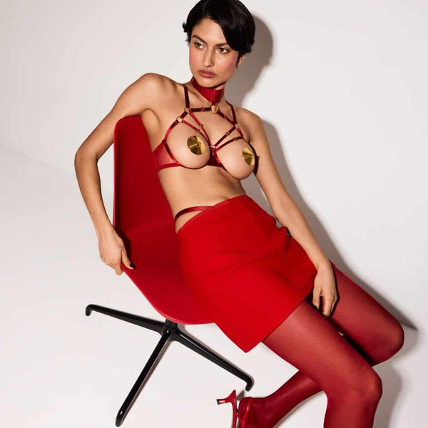 Femme Assise portant un Soutien-Gorge Ouvert, un String en Résille, des Bas et une Jupe couleur Rouge et des Nippies dorés