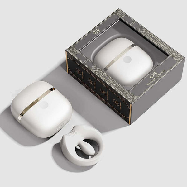 Cockring connecté APIS présenté avec son étui de recharge, câble USB et carte de garantie, disposés sur fond clair dans une mise en scène minimaliste et élégante.