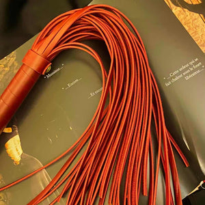 Fouet rouge BDSM posé sur un décor avec des écritures