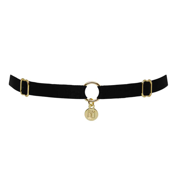 Ici vous pouvez voir le BRIGADE MONDAINE GIFT WRAP BLACK. Ce collier est fait d’une bande noire. 2 détails pour régler les bandes se trouvent à droite et à gauche. Au milieu, la bande est séparée par un anneau plaqué or avec un pendentif ou il est inscrit « BM ».