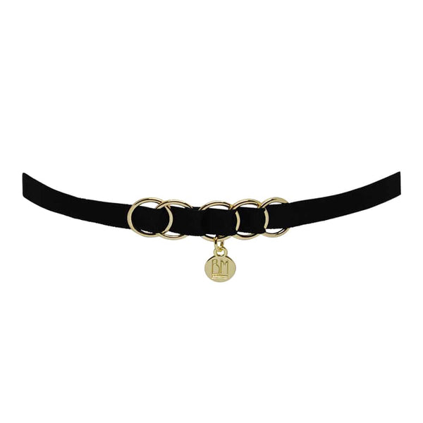 Ici vous pouvez voir le BRIGADE MONDAINE GIFT WRAP BLACK. Ce collier est fait d’une bande noire. 5 anneaux se trouvent au milieu et traversent la bande. Un détail de forme ronde avec écrit « BM » pend au milieu.