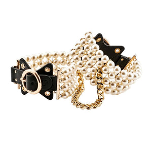 Entraves de chevilles en cuir noir ornées de perles et reliées par une chaîne dorée, portées sur modèle, proposées par Brigade Mondaine Paris.
