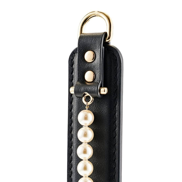 Paddle BDSM en cuir noir avec finition lisse et rangée de perles décoratives, tenu par un modèle en studio, accessoire sélectionné par Brigade Mondaine Paris.