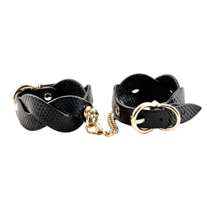 Modèle portant des menottes BDSM noires pour poignets avec chaîne dorée, accessoire de contrainte proposé par Brigade Mondaine Paris.