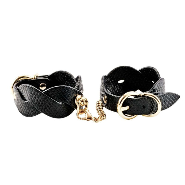 Modèle portant des menottes BDSM noires pour poignets avec chaîne dorée, accessoire de contrainte proposé par Brigade Mondaine Paris.