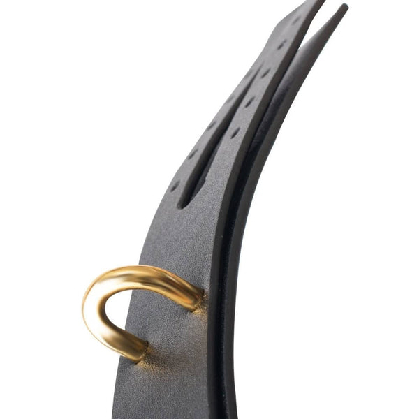 Menottes de chevilles BDSM en cuir noir avec boucle métallique et chaîne dorée, portées aux chevilles avec escarpins noirs à talons, photographiées sur fond gris.