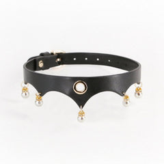 Gros plan d’un collier BDSM en cuir noir porté au cou, orné d’anneaux dorés et de perles blanches, sur fond sombre, dans une esthétique élégante et minimaliste.