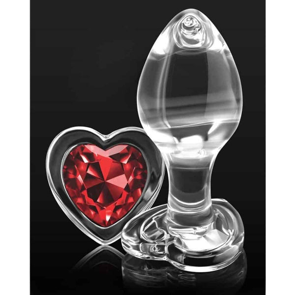 Plug anal en cristal transparent posé sur fond noir, avec une base décorative en forme de cœur rouge facetté, à l’esthétique élégante et raffinée.