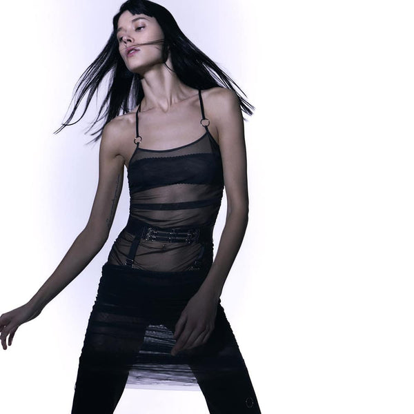 Ensemble Top et jupe Les Indolentes Collection Caravasar de la marque Gonzales Affaires. Cette jupe s’arrête en dessous des genoux. Le produit est confectionné à partir d’une partie en tulle transparent gris des genoux jusqu’au nombril. Une couture est située sur le côté de la robe afin d’obtenir ou non un rendu plissée de la jupe en saisissant l’anneau au bout de la jupe. Ensuite une ceinture est placée au niveau des hanches avec trois élastiques fins ornés d’anneaux argenté au centre de la ceinture. Les d