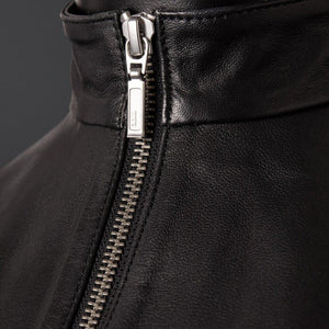 Top en cuir de mouton noir zippé à col montant zip central et dos entièrement ouvert à nouer La coupe est droite, couvrante. La matière, elle, ne cache rien.