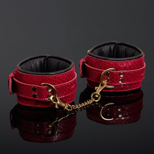 Menottes en cuir embossé serpent rouge avec finitions dorées et intérieur en cuir de veau noir, offrant confort et maintien avec un design visuellement saisissant.