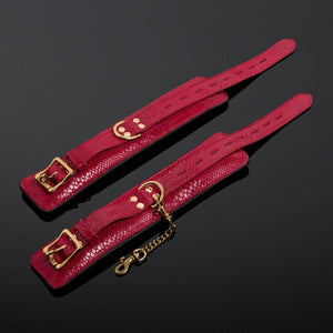 Menottes en cuir embossé serpent rouge avec finitions dorées et intérieur en cuir de veau noir, offrant confort et maintien avec un design visuellement saisissant.