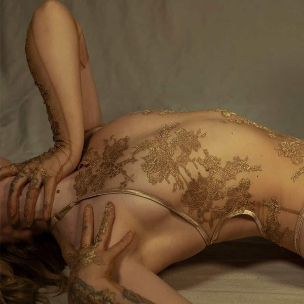 Le body licou AMMALIE sublime la silhouette avec son effet seconde peau et son éclat doré subtil. Confectionné à la main en maille illusion ultra-transparente, il épouse le corps avec finesse. Son appliqué en dentelle Leavers française en or rosé, découpé et cousu à la main, ajoute une touche précieuse. Les bretelles dorées réglables et les accessoires plaqués or 24 carats assurent un ajustement parfait. Pour un confort optimal, l’intérieur est doublé en coton de bambou biologique.