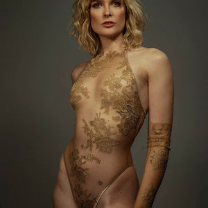 Le body licou AMMALIE sublime la silhouette avec son effet seconde peau et son éclat doré subtil. Confectionné à la main en maille illusion ultra-transparente, il épouse le corps avec finesse. Son appliqué en dentelle Leavers française en or rosé, découpé et cousu à la main, ajoute une touche précieuse. Les bretelles dorées réglables et les accessoires plaqués or 24 carats assurent un ajustement parfait. Pour un confort optimal, l’intérieur est doublé en coton de bambou biologique.