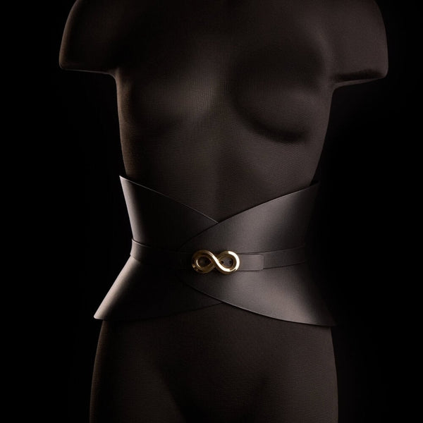 Corset ceinture HUDIA IINFYNII en cuir noir avec fermoir métallique infini porté sur un tailleur noir, accessoire structurant et graphique proposé par Brigade Mondaine Paris