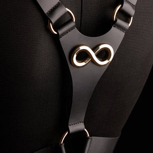 Harnais TRISCA IINFYNII en sangles noires avec boucles dorées et détail central, accessoire structurant porté sur le buste proposé par Brigade Mondaine Paris