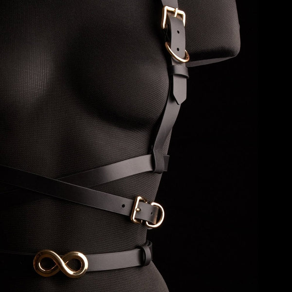 Harnais TRISCA IINFYNII en sangles noires avec boucles dorées et détail central, accessoire structurant porté sur le buste proposé par Brigade Mondaine Paris