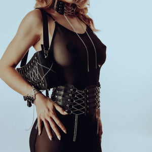 Ceinture corset en cuir et acier inoxydable avec fermeture ajustable, chaîne amovible. Choker en cuir d’agneau avec anneaux en argent sterling. Sac à main en cuir avec design corset argenté, pompom en cuir, intérieur en daim violet.