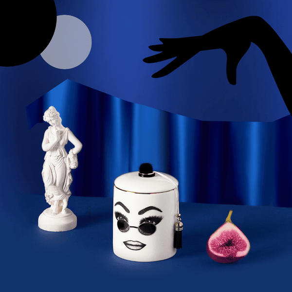 Une bougie parfumée en porcelaine de Chine blanche arbore un visage confiant, soigneusement tracé en feutrine. Ce visage exprime la la confiance en soi, le confort et le cool avec des lunettes de soleils rondes et un maquillage parfaitement exécuté.