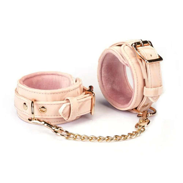 Menottes Boudoir Amor en similicuir vegan rose pastel et noir. Finitions dorées, anneau en D pour fixation. Boucles ajustables et clips à dégagement rapide pour sécurité et confort. Idéales pour des jeux de soumission élégants.