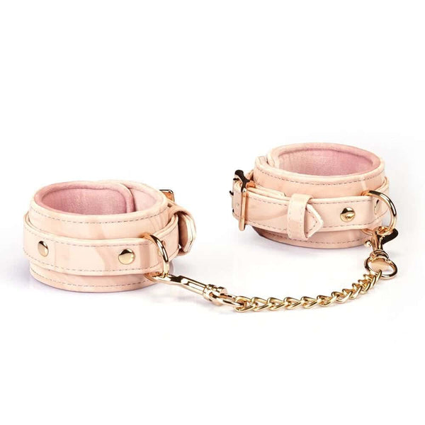 Menottes Boudoir Amor en similicuir vegan rose pastel et noir. Finitions dorées, anneau en D pour fixation. Boucles ajustables et clips à dégagement rapide pour sécurité et confort. Idéales pour des jeux de soumission élégants.