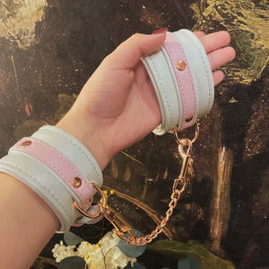Menottes de bondage FAIRY en cuir blanc et rose avec accents or rose. Ajustables avec boucles métalliques et clips à dégagement rapide pour un ajustement sécurisé et confortable. Parfaites pour les jeux BDSM.