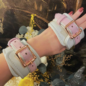 Menottes de bondage FAIRY en cuir blanc et rose avec accents or rose. Ajustables avec boucles métalliques et clips à dégagement rapide pour un ajustement sécurisé et confortable. Parfaites pour les jeux BDSM.