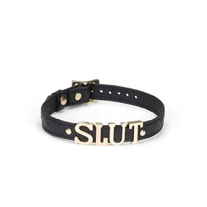 Choker en cuir noir embossé avec lettres argentées SLUT et finitions dorées. Accessoire ajustable, souple et confortable, parfait pour jeux BDSM et tenues fétichistes.