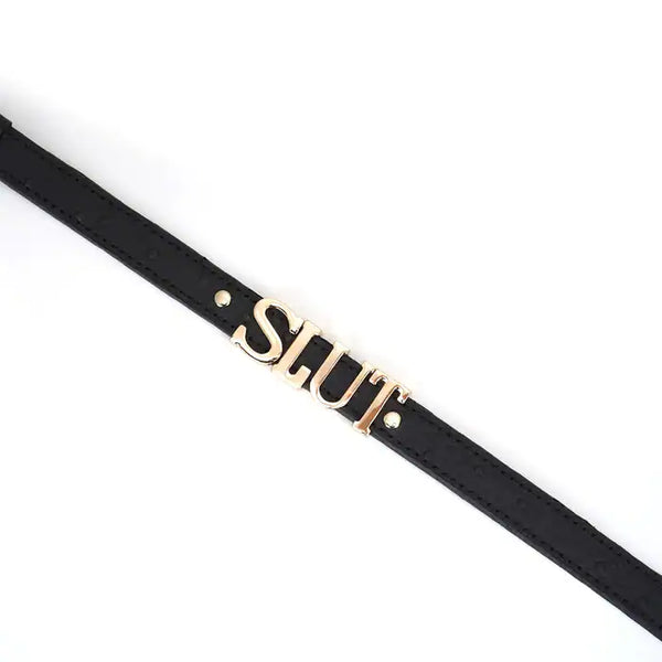 Choker en cuir noir embossé avec lettres argentées SLUT et finitions dorées. Accessoire ajustable, souple et confortable, parfait pour jeux BDSM et tenues fétichistes.