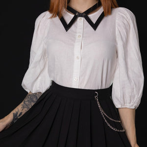 Choker 86647 en cuir noir, porté avec une chemise blanche et une jupe noire à détails argentés. Confectionné à la main, avec des vis à l’avant rappelant les boutons d’un col et une boucle réglable à l’arrière.