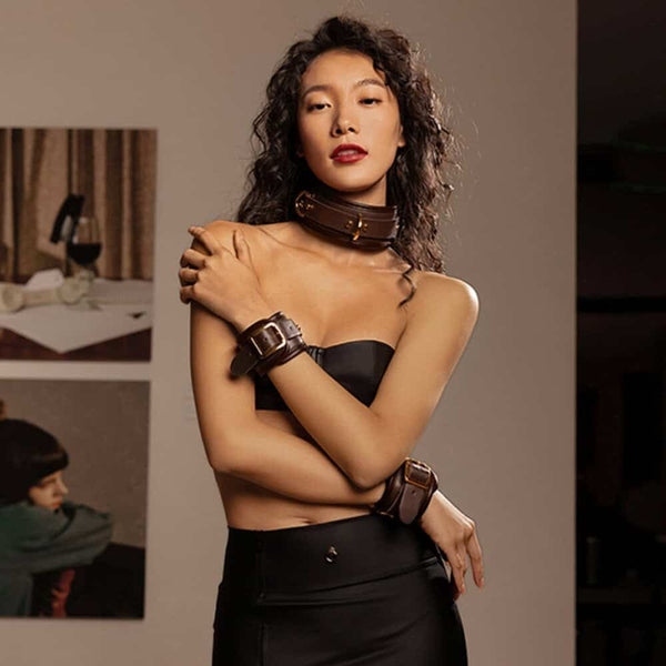 Collier et menottes de poignets UPKO en cuir brun avec boucles métalliques dorées, portés avec une tenue noire, sélection Brigade Mondaine Paris