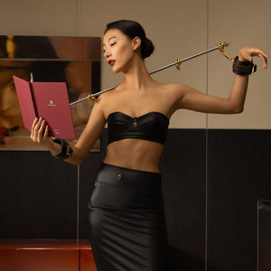 Accessoires BDSM en cuir noir avec menottes et barre rigide en métal doré, design haut de gamme disponible chez Brigade Mondaine Paris
