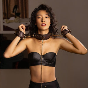 Collier et menottes UPKO en cuir brun reliés par une chaîne en métal doré portée à l’avant, sélection Brigade Mondaine Paris
