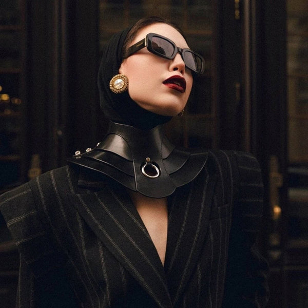 Mannequin portant le collier Posture Hold en cuir noir RE:STRICT chez Brigade Mondaine Paris, pièce rigide couvrant le cou, anneau métallique central, porté avec un top en mesh noir en studio.