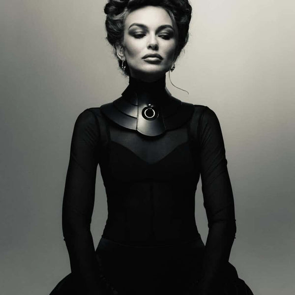 Mannequin portant le collier Posture Hold en cuir noir RE:STRICT chez Brigade Mondaine Paris, pièce rigide couvrant le cou, anneau métallique central, porté avec un top en mesh noir en studio.