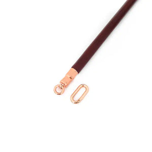 Barre d’écartement en cuir rouge vin avec noyau en bois d’eucalyptus. Joints toriques en métal or rose pour fixer des chevillières. Élégante et fonctionnelle pour des jeux BDSM raffinés.