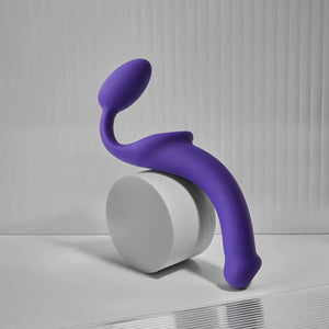 Plug strapless violet STRAP-ON-ME au design courbé et ergonomique, posé sur un socle minimaliste, sélection Brigade Mondaine Paris.