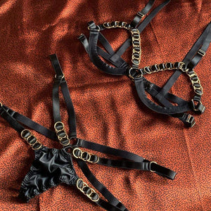 Ensemble soutien gorge et string noir très sexy, ouvert au niveau des seins et des hanches. L'ensemble est décoré avec des ronds dorés
