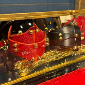Bracelet Horizontal en cuir Rouge Cherry et Noir signé Úna Burke, avec raccords en laiton massif recouverts d'or et vis en laiton, combinant l'esthétique rock chic et bondage pour une pièce élégante et audacieuse.