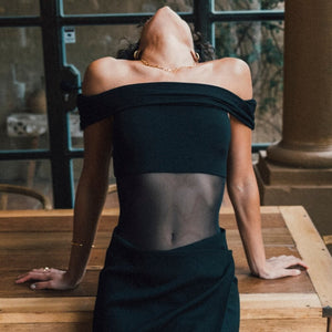 Body noir Undress Code Libra à épaules dégagées, porté par un modèle tenant une coupe de champagne, sélection Brigade Mondaine Paris.