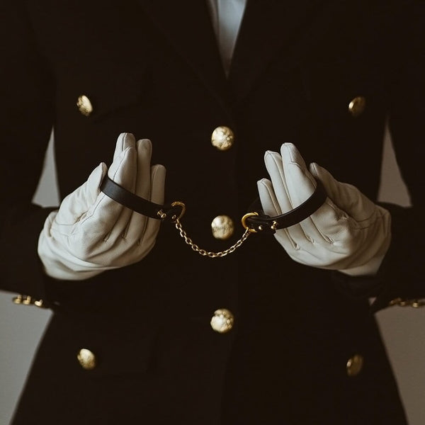 Menottes UPKO en cuir noir avec chaîne dorée, portées sur gants blancs, sélection Brigade Mondaine Paris