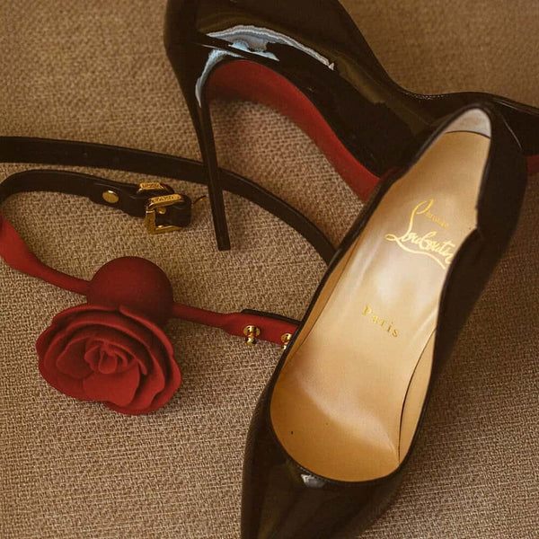 Gag UPKO en forme de fleur rouge fixé sur un escarpin noir à semelle rouge, disponible chez Brigade Mondaine Paris