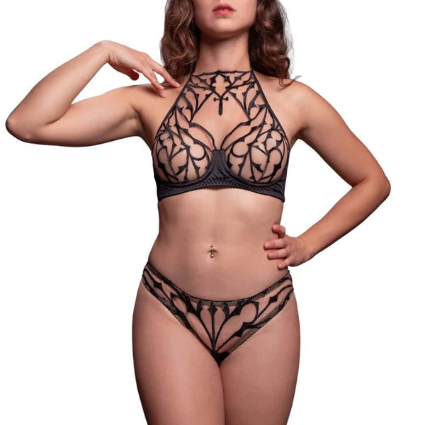 Mannequin portant la culotte tanga Dogma VIDE NOIR chez Brigade Mondaine Paris, dentelle noire ajourée aux motifs graphiques, coupe échancrée, porté avec un soutien-gorge assorti, photographié en studio.