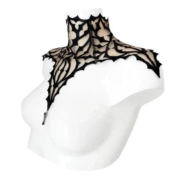 Plastron gothique brodé noir sur tulle nude, orné d’un pendentif central. Forme montante couvrant cou et épaules. Fermeture réglable par ruban façon corset au dos.