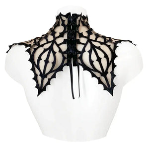 Plastron gothique brodé noir sur tulle nude, orné d’un pendentif central. Forme montante couvrant cou et épaules. Fermeture réglable par ruban façon corset au dos.