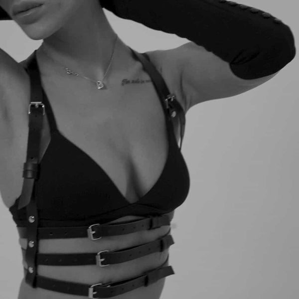 Femme en noir et blanc portant un harnais en cuir naturel fait à la main, avec trois lanières sous le buste et deux lanières montant vers le cou, créant un effet de soutien-gorge. Elle porte également un soutien-gorge noir, et le cuir est mis en valeur par la lumière, accentuant la texture et le design sophistiqué.